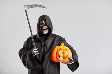Portrait of the grim reaper, holding a pumpkin and scythe, wearing skeleton costume standing on a...