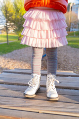 joyful child on wooden platform at playground, pink fluffy skirt, white patent leather boots, autumn nature, Childhood joy, Playful moment