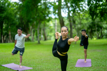 Three people are doing yoga on a green mat in a park