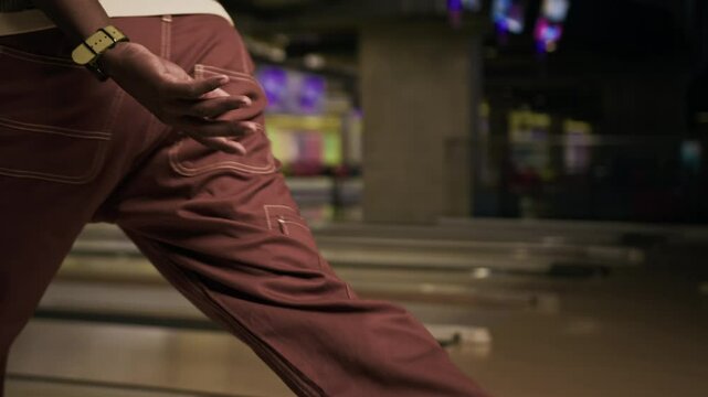 Tilt up of cheerful Black guy throwing bowling ball on lane while hanging out together with friends