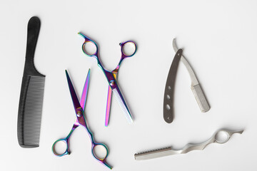 A detailed aerial view of barber tools on a white backdrop. Scissors, clippers, razors, and brushes are centrally placed