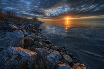 Obraz premium A serene scene of a sunset over a body of water with rocks in the foreground, perfect for use in travel or nature-related projects
