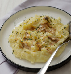 A plate of creamy mashed potatoes topped with a rich, savory gravy and garnished with fresh herbs. The dish is served on a white plate, with a spoon placed on the side, ready to be enjoyed