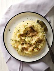 A plate of creamy mashed potatoes topped with a rich, savory gravy and garnished with fresh herbs. The dish is served on a white plate, with a spoon placed on the side, ready to be enjoyed