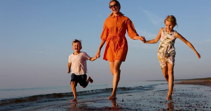 happy mother with kids running on the baltic sea beach coast at sunset