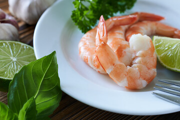 Shrimps on a white plate with lime and basil on a wooden table