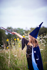 Caucasian blonde child girl in wizard blue costume with cape and hat, casting a spell with magic...