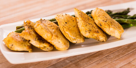 Fried chicken breast pieces with asparagus on white plate