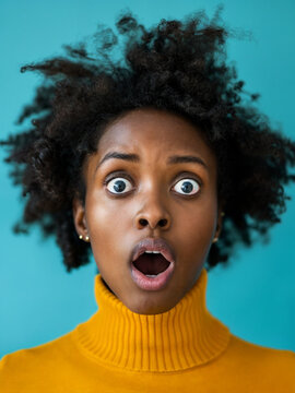 A black woman in a yellow sweater has her mouth open wide and is staring with her eyes wide open.