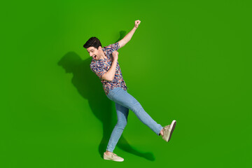 Full size photo of overjoyed guy dressed print shirt jeans dancing having fun look down empty space isolated on green color background