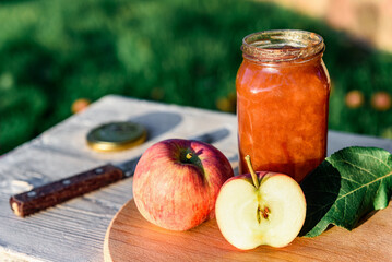 Glass jar of apple jam and fresh fruits on garden background.