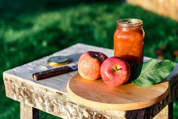 Glass jar of apple jam and fresh fruits on garden background.