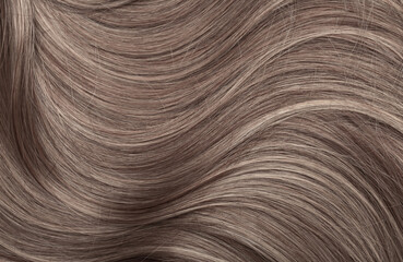 Blond hair close-up as a background. Women's long light brown hair. Beautifully styled wavy shiny curls. Hair coloring. Hairdressing procedures, extension.