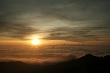 Sunrise over the mountains. Warm colors over a sea of clouds with silhouette of mountains on the horizon. 