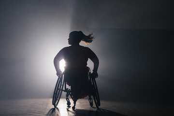 Graceful wheelchair dance of a woman with a disability on a black background with bright backlight. Para dance concept.