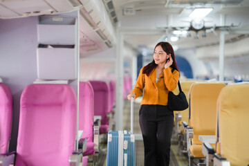 Finding Her Seat: A young Asian woman navigates the aisle of an airplane, her rolling suitcase trailing behind her as she prepares for takeoff and the adventures that await.  © Wicitr