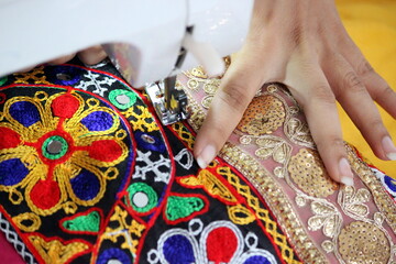 stitching machine closeup for sewing the floral design traditional navratri laces for chaniya choli. dress is getting ready by a tailor. stitching business for navratri festival in gujarat india. 