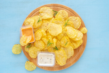 Potato chips served with fresh rosemary and tartar sauce and pink sauce on blue wooden background.
