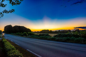 A car speeding freely on a rural road going through fields with a lovely rural sunset in the background © Chris