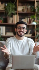 A happy young handsome man wearing glasses and white shirt talking to camera doing video call, sitting on sofa in modern living room at home office, library