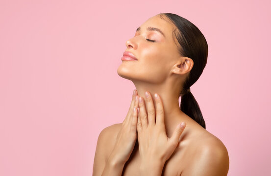 Attractive adorable serene young woman touching pure neck skin isolated over pink background, free space