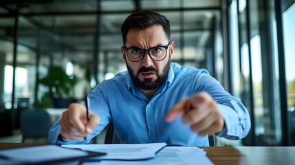 Obraz premium An angry boss in an office, pointing at the camera with his finger, sitting behind a desk and holding papers