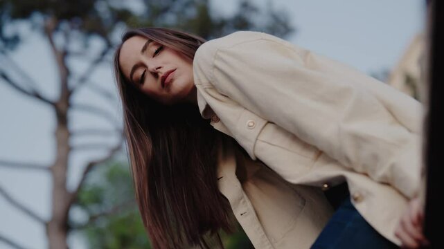 Stylish young woman in a beige coat posing outdoors with her eyes closed and her head tilted. Gentle expression in a natural, soft light setting. Portrait of a Young Woman in a Beige Coat Outdoors