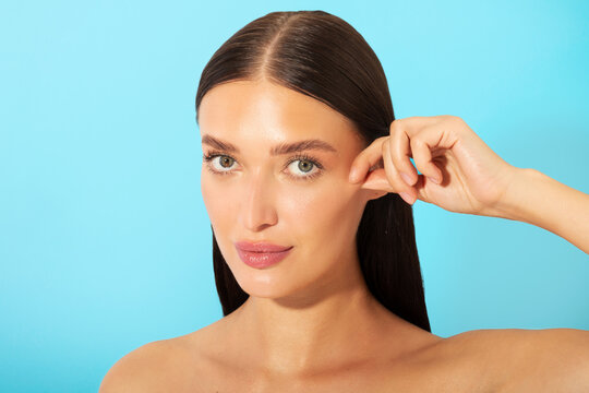Skin firming concept. Beautiful young lady with flawless tight skin touching her cheek and looking at camera, posing over blue studio background