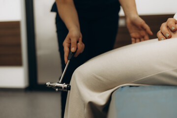 Doctor knocks a hammer on the knee of a girl, checking reflexes at a doctor's appointment