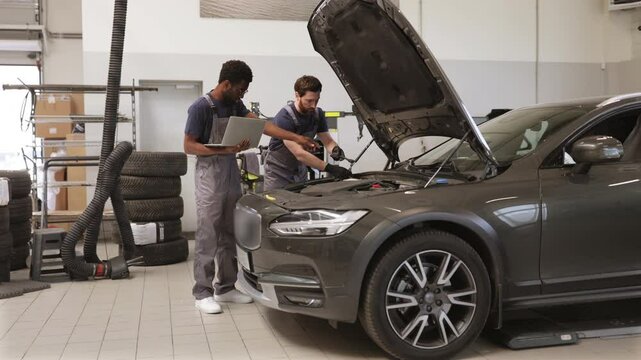 Two auto mechanics inspecting car engine in workshop environment. Professionals diagnosing vehicle with laptop and tools. Automotive maintenance, repair, and teamwork concept