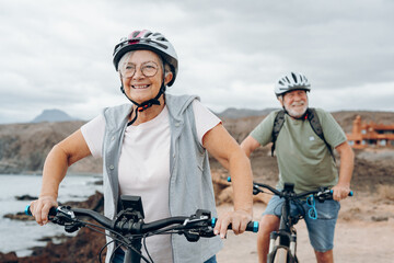 Senior couple riding bikes together in rocky beach enjoying outdoor. Active mature people talking...