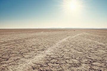 Expansive dry landscape under a clear blue sky, showing cracked earth and the bright sun illuminating the barren terrain.