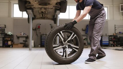 Mechanic changing car tire in professional auto repair shop. Worker in uniform handling tire for maintenance and repair. Automotive service concept captured in garage environment.