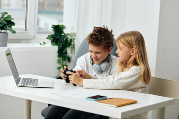 Fototapeta premium Happy Boy and Girl Studying Online with Laptops at Home Two Caucasian children, a boy and a girl, are sitting at a table in their cozy living room They are wearing headphones and concentrating on