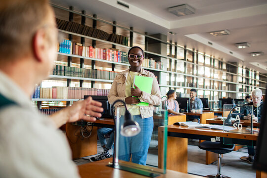 Smiling female black student returning paper to professor in college library