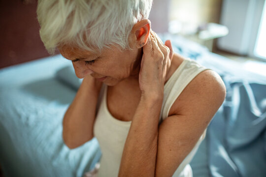 Senior woman holding neck in pain on bed at home