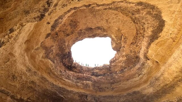 View of Banagil Cave in Albufeira in the Algarve region of Portugal.People look at the cave hole in the top and the swallows fly. Natural rock formation