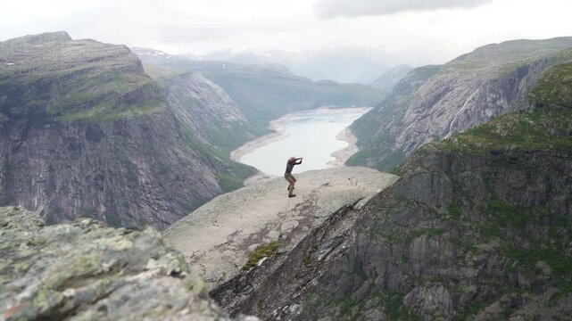 Fencer doing Shadow Fight with long medieval metal historical sword on famous Trolltunga "Troll's Tongue" cliff over Ringedalsvatnet lake. Trolltunga trek final point in Norway. Active man 4K video