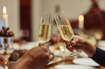 Glass, hands and toast with couple at dining room table in home for celebration at Christmas. Champagne, cheers and festive with people in apartment for drinking, event or social gathering closeup