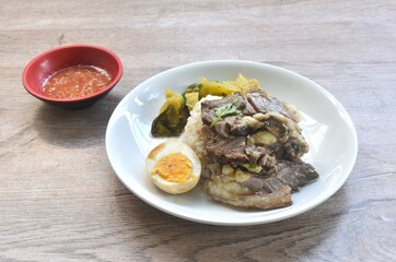 braised  slice beef stew black Chinese herb soup topping brown boiled egg half cutting eat couple pickled cabbage dipping spicy sour chili sauce on plain rice in plate 