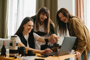 Young female photographer in photo studio shows photos on laptop to model and assistant.