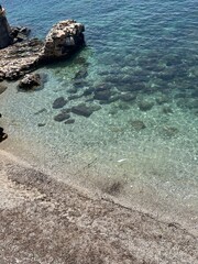A serene shoreline with smooth pebbles and rocks meeting clear, turquoise water, highlighting the...