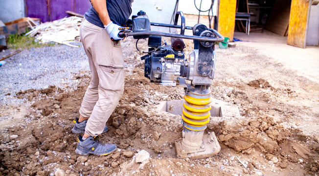 Compacting the soil. A compacting machine in the process of manual operation. Compacting the soil to build a foundation. Construction workers, rammer, worker with rammer.