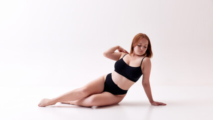 Uniqueness. Beautiful young woman with natural body posing in black underwear in floor isolated on white studio background. Concept of female beauty, body positivity, care, acceptance