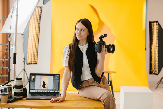 Portrait of a female photographer with a camera in her hands against the background of the interior of a photo studio.
