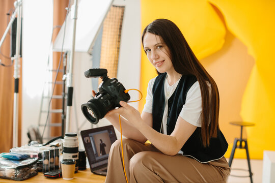 Portrait of a studio photographer at work. A beautiful brunette woman holds a professional camera in her hands and smiles.