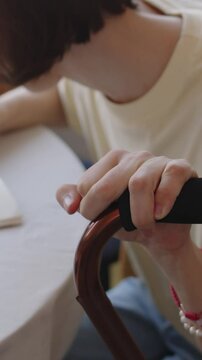 Vertical of Caucasian teenage girl with cerebral palsy sitting at table with walking stick and drawing or writing in copybook