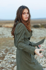 Serene woman in green trench coat embracing nature on rocky hilltop in peaceful solitude