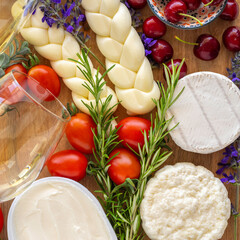 Cheese board for Jewish holiday Shavuot, for Harvest. Camembert, cottage cheese, braided mozzarella, fresh rosemary, tomatoes on wooden background.
