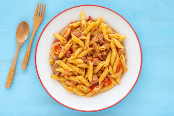 Tuna Pasta with tomatoes on ceramic plate over blue wooden background.
